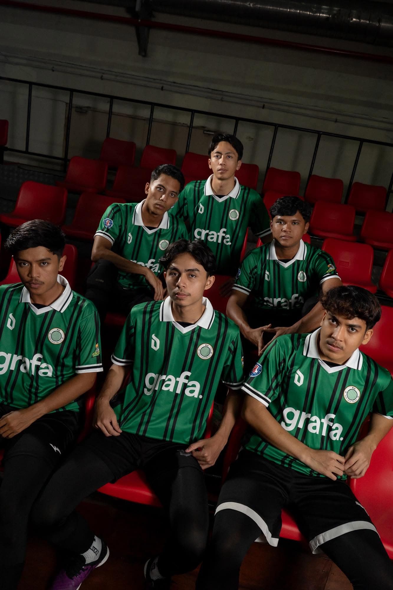 Seven Petaling Jaya Juara players in the green pinstriped home kit, seated on red stadium seats